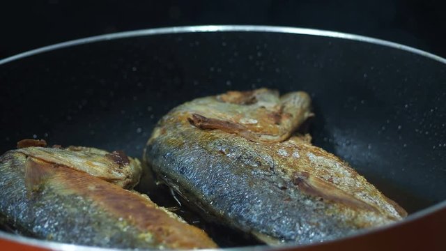 Two mackerel are fried in a pan with hot oil.