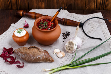 Rustic still life with borsch in a clay pot, green onions and bread