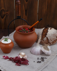 Rustic still life with borsch in a clay pot, green onions and bread