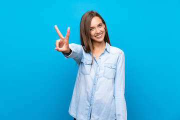 Young woman over isolated blue background smiling and showing victory sign