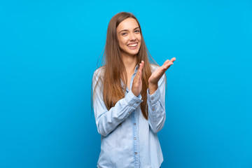 Young woman over isolated blue background applauding after presentation in a conference