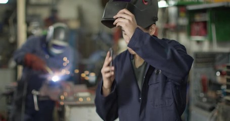 4K Young mechanic in garage workshop having a friendly conversation on the phone