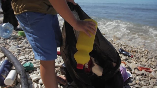 Environmental pollution problem, ecological disaster, volunteering and recycling. Close up shot of child cleaning up beach with plastic bags full of garbage on seashore. Care for future generations