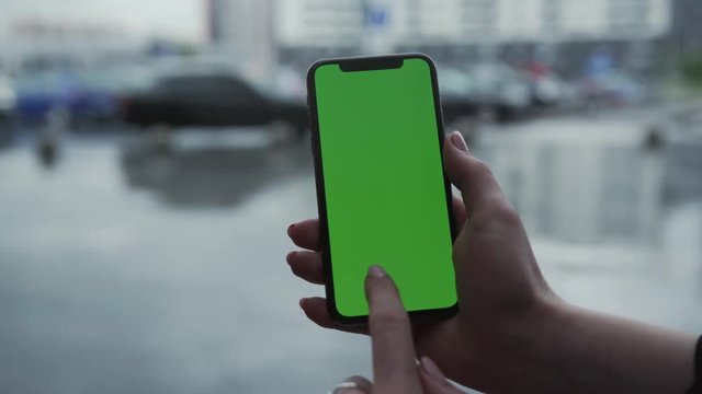 Los Angeles, California - 5 April 2019: Woman hand holding vertically smart phone cellphone with green screen background rain parking cars weather app cellphone outside rain trees raindrops