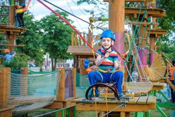 Little cute boy enjoying activity in a climbing adventure park on a summer sunny day. toddler climbing in a rope playground structure.