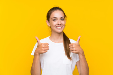 Young woman over isolated yellow background giving a thumbs up gesture