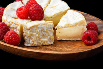 camembert soft cheese with raspberries on wood background. French food. macro shot.