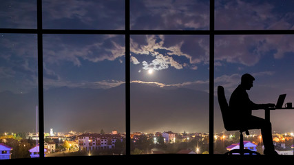 The silhouette of working man near window on the night city background