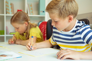 Fototapeta premium Cute schoolchildren are came back to school and learning at the table in classroom