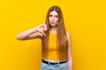 Young woman over isolated yellow background showing thumb down sign