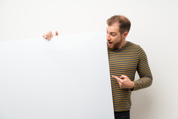 Handsome man over isolated white wall holding an empty white placard for insert a concept