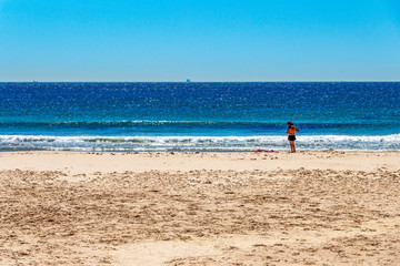 A couple at the empty Playa de los Lances or Los Lances Beach, silhouette of a fishing boat in the...