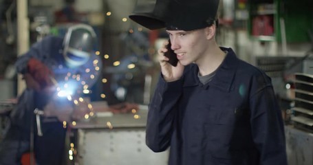 4K Young mechanic in garage workshop having a friendly conversation on the phone