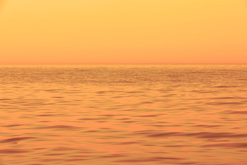 Fototapeta premium Abstract horizontal theme by means of waves, water, skyline, and sky during golden sunset. Soft pastel detail of sea waves. Out of focus and blurred. Soft focus