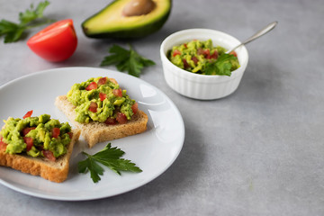 Toasts with an avocado snack and fresh vegetables on a gray background.