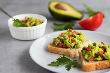 Toasts with an avocado snack and fresh vegetables on a gray background.