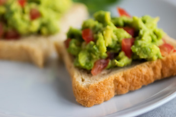 Toasts with an avocado snack and fresh vegetables on a gray background.