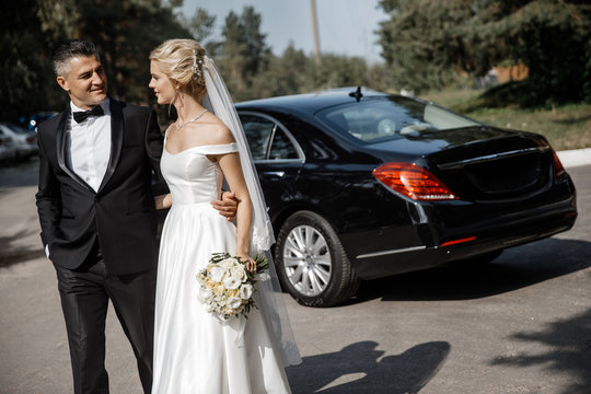 A Bride And A Groom Are Walking Away From A Car Together.