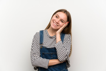 Fototapeta premium Young woman in dungarees over white wall laughing