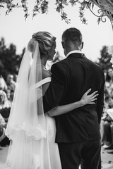 A bride and a groom are hugging in front of the guests. Black and white picture.