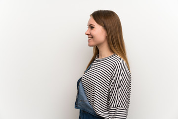 Young woman in dungarees over white wall standing and looking to the side