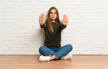 Young woman sitting on the floor making stop gesture and disappointed