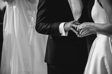 A bride and a groom are putting the rings on each others fingers. Black and white image.