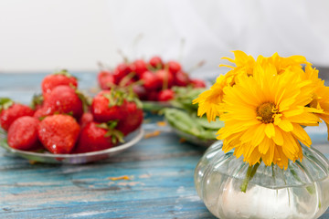 Bouquet of yellow-orange flowers in a glass vase, in the background strawberries and sweet cherry
