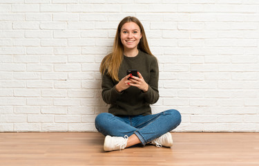 Young woman sitting on the floor sending a message with the mobile