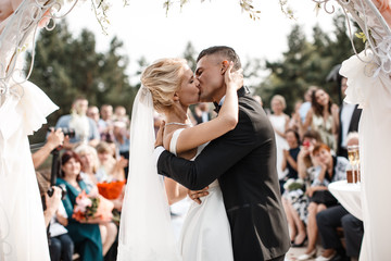 A bride and a groom are kissing in front of the guests. - Powered by Adobe