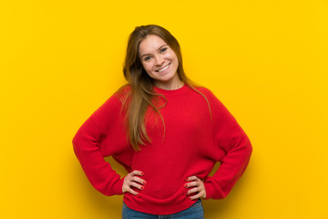 Obraz premium Young woman over yellow wall posing with arms at hip and smiling