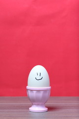 Boiled egg in poached pink. On the egg painted smiley. Against the background of coral color.