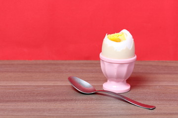 Boiled egg in poached pink. Next spoon for food. Against the background of coral color.