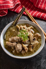 Soup with pieces of pork and mushrooms in bowl.