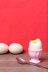 Boiled egg in poached pink. Next spoon for food. Against the background of coral color.