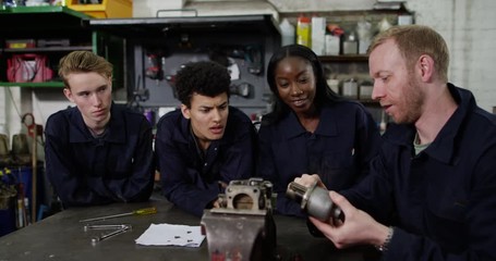 4K Mechanics students listening to teacher explaining in garage workshop. Slow motion.