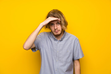 Blonde man over isolated yellow background looking far away with hand to look something