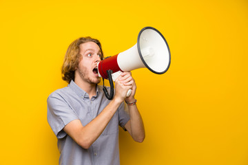 Blonde man over isolated yellow background shouting through a megaphone