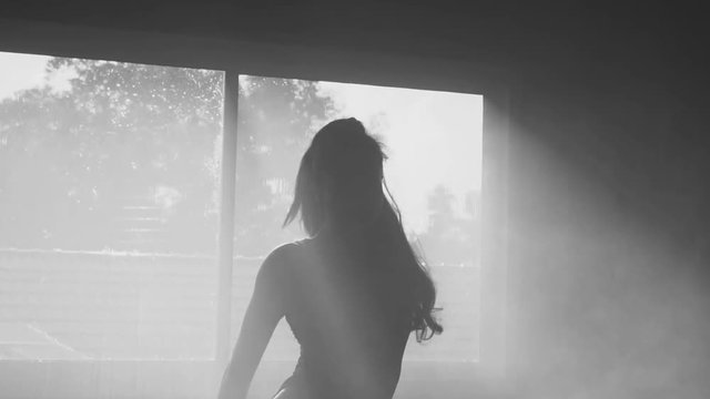 Silhouette of beautiful sensual woman in body suit dancing in hazy studio over window view background - black and white video in slow motion