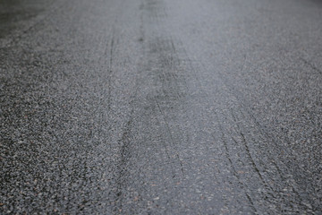 Wet asphalt road on a rainy day. Tilted angle, focused on the foreground. High resolution full frame background.