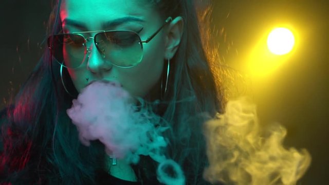 Gorgeous brunette woman smoking electronic cigarette in neon color light - video in slow motion