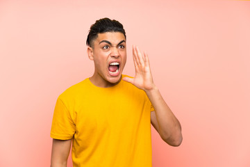 Young man with yellow shirt over isolated pink wall shouting with mouth wide open