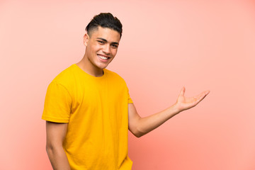Young man with yellow shirt over isolated pink wall holding copyspace imaginary on the palm