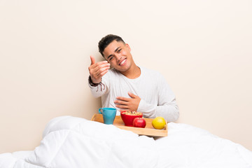 Young man having breakfast in bed inviting to come