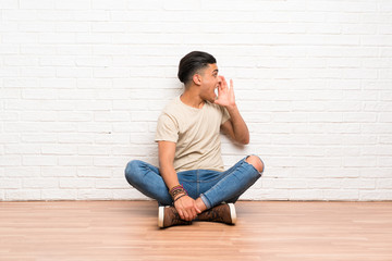 Young man sitting on the floor shouting with mouth wide open