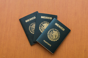 Tres pasaportes mexicanos apilados sobre mesa de madera. Vista desde arriba.
