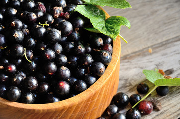 Black currant in a wooden bowl on the background of old boards, top view.