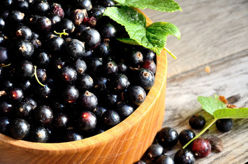 Black currant in a wooden bowl on the background of old boards, top view.