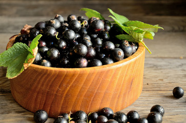 Harvest, ripe black currants, in a wooden bowl on old wooden boards.