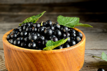 Harvest, ripe black currants, in a wooden bowl on old wooden boards.